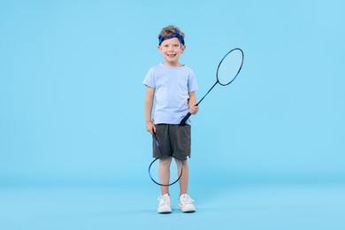 Photo of Little boy with badminton rackets on light blue background