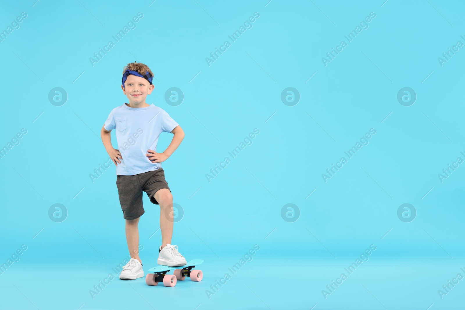 Little boy with penny board on light blue background, space for text Photo of Little boy with penny board on light blue background, space for text