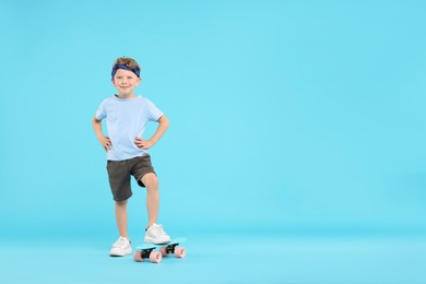 Photo of Little boy with penny board on light blue background, space for text