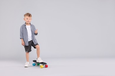 Photo of Little boy with penny board showing thumbs up on gray background, space for text