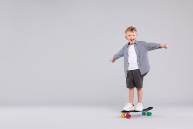 Photo of Cheerful little boy standing on penny board and showing thumbs up against gray background, space for text