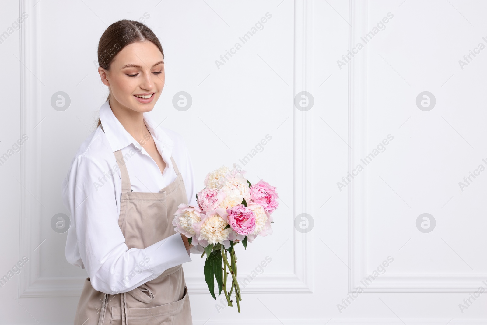 Florist with beautiful bouquet of peonies near white wall indoors, space for text Photo of Florist with beautiful bouquet of peonies near white wall indoors, space for text