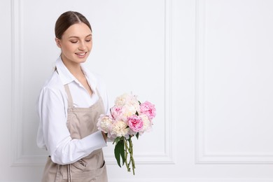 Photo of Florist with beautiful bouquet of peonies near white wall indoors, space for text
