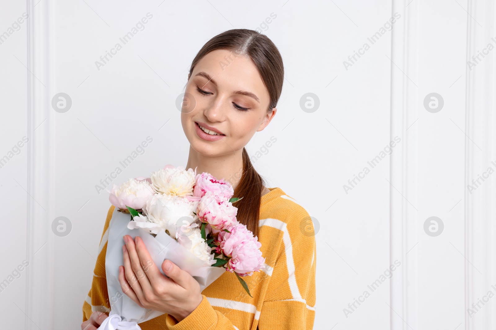 Woman with beautiful bouquet of peonies near white wall indoors, space for text Photo of Woman with beautiful bouquet of peonies near white wall indoors, space for text