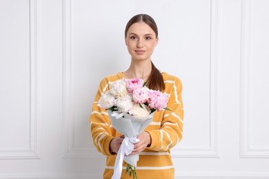 Photo of Woman with beautiful bouquet of peonies near white wall indoors