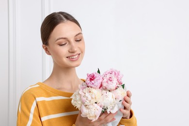 Photo of Woman with beautiful bouquet of peonies near white wall indoors, space for text