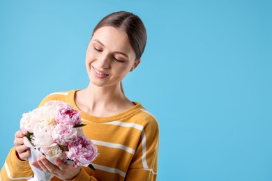Photo of Woman with beautiful bouquet of peonies on light blue background, space for text
