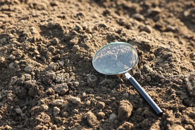 Photo of Magnifying glass on dry soil in field, space for text