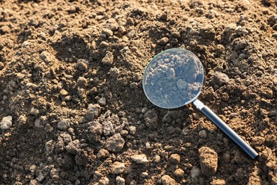 Photo of Magnifying glass on dry soil in field, above view. Space for text