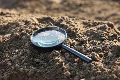 Photo of Magnifying glass on dry soil in field, closeup