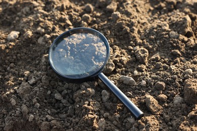 Photo of Magnifying glass on dry soil in field, closeup