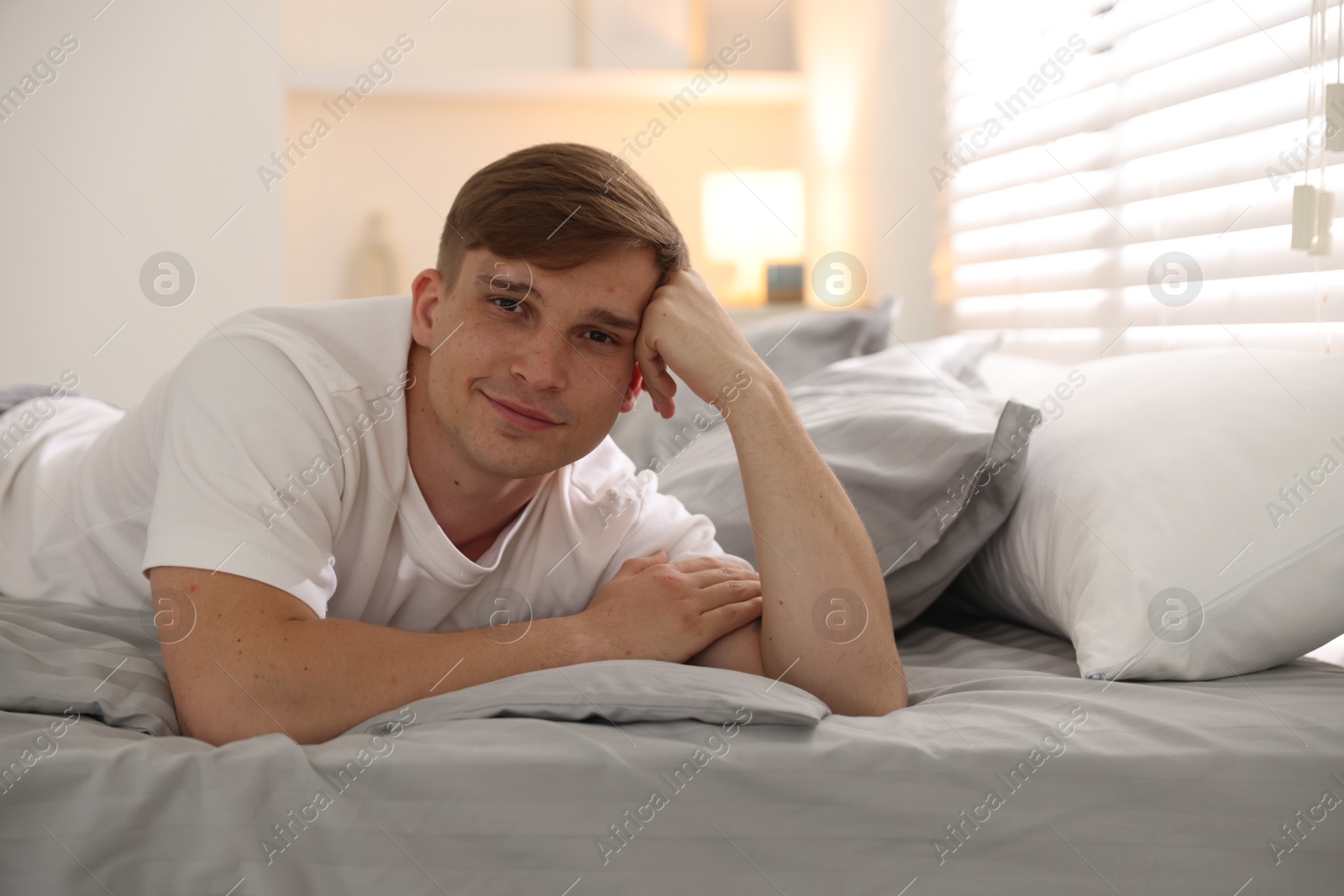 Young man lying on bed with soft mattress at home, space for text Photo of Young man lying on bed with soft mattress at home, space for text