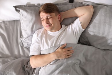 Photo of Young man sleeping on bed with soft mattress at home, top view