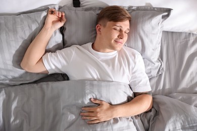 Photo of Young man sleeping on bed with soft mattress at home, top view