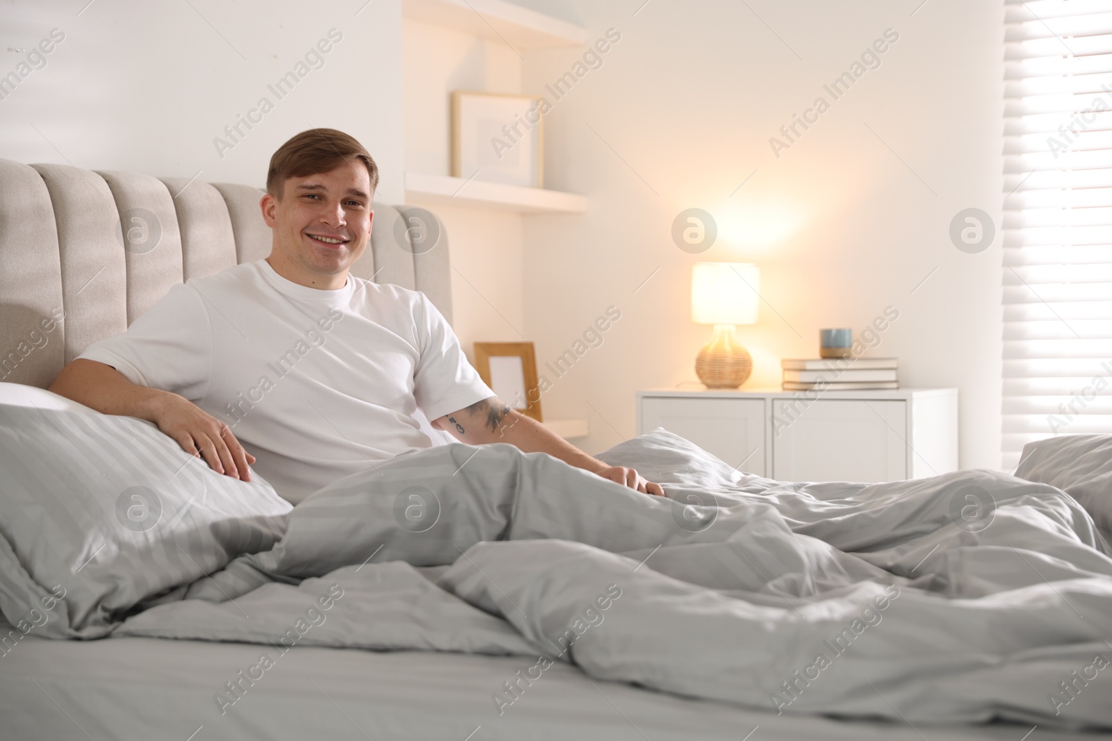 Young man stretching on bed with soft mattress at home Photo of Young man stretching on bed with soft mattress at home