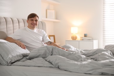 Photo of Young man stretching on bed with soft mattress at home