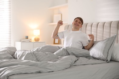 Photo of Young man stretching on bed with soft mattress at home
