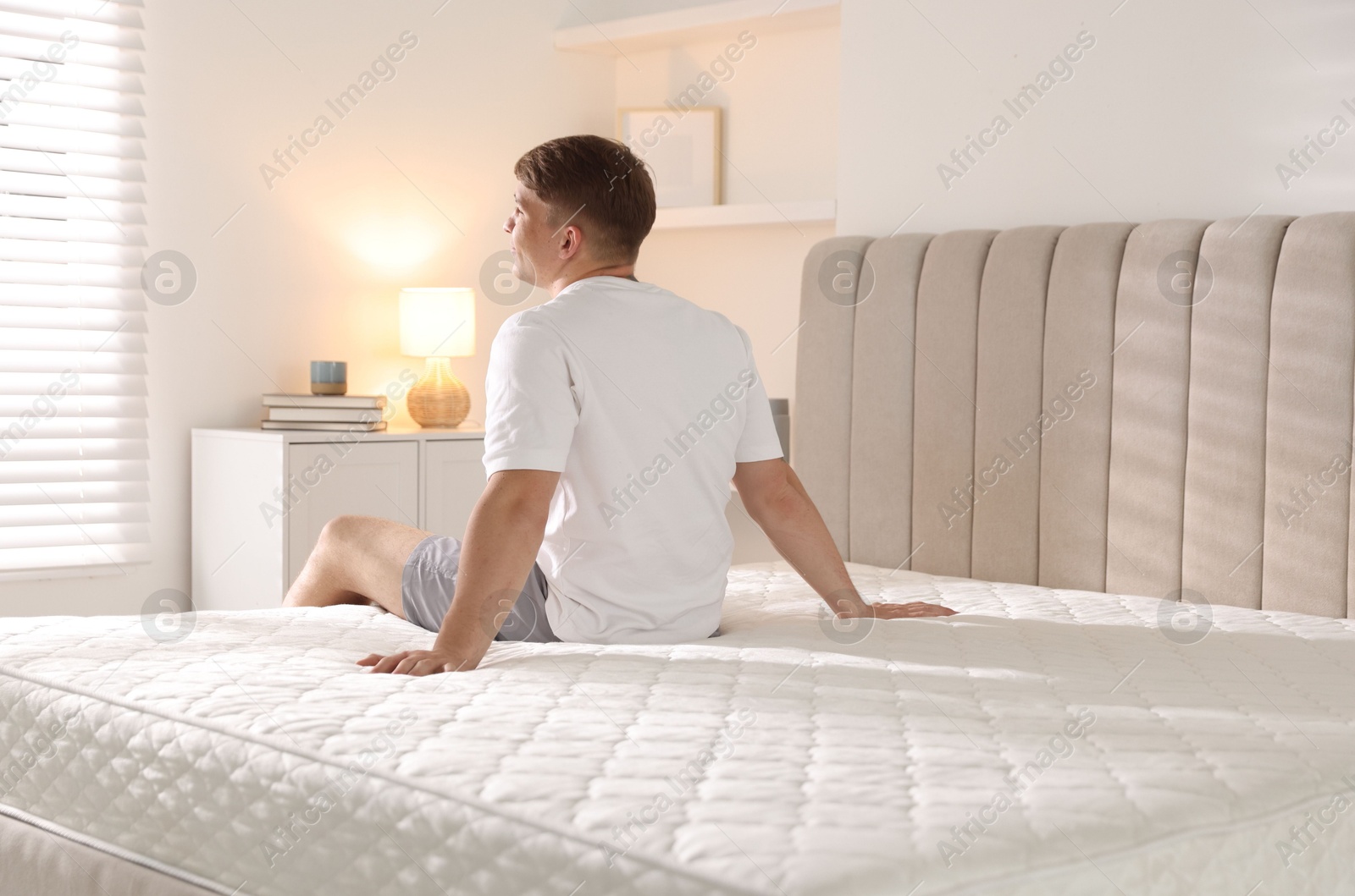 Young man sitting on bed with soft mattress at home, back view Photo of Young man sitting on bed with soft mattress at home, back view