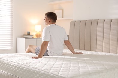 Photo of Young man sitting on bed with soft mattress at home, back view