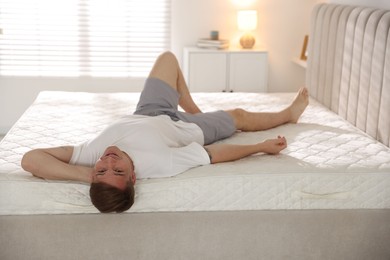Photo of Young man lying on bed with soft mattress at home