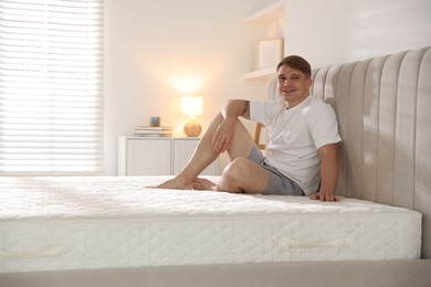 Photo of Young man sitting on bed with soft mattress at home, space for text