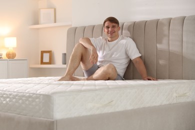 Photo of Young man sitting on bed with soft mattress at home