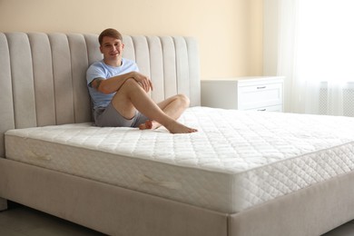Photo of Young man sitting on bed with soft mattress at home, space for text