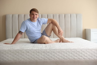 Photo of Young man sitting on bed with soft mattress at home
