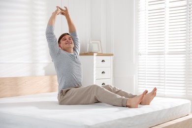 Photo of Young man stretching on bed with soft mattress at home