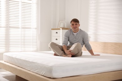 Photo of Young man sitting on bed with soft mattress at home