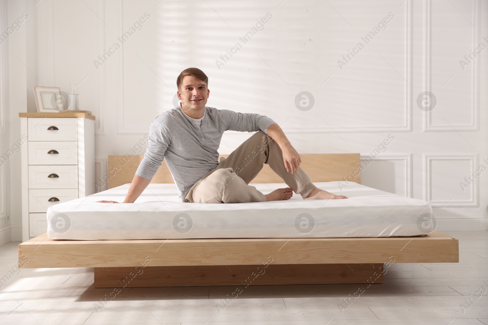 Young man sitting on bed with soft mattress at home Photo of Young man sitting on bed with soft mattress at home