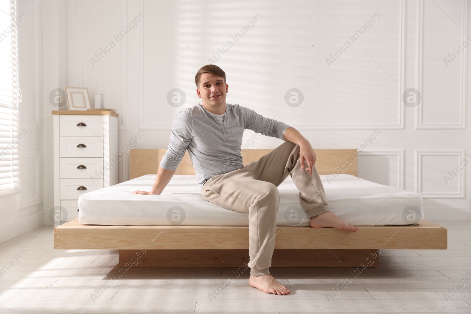 Young man sitting on bed with soft mattress at home Photo of Young man sitting on bed with soft mattress at home