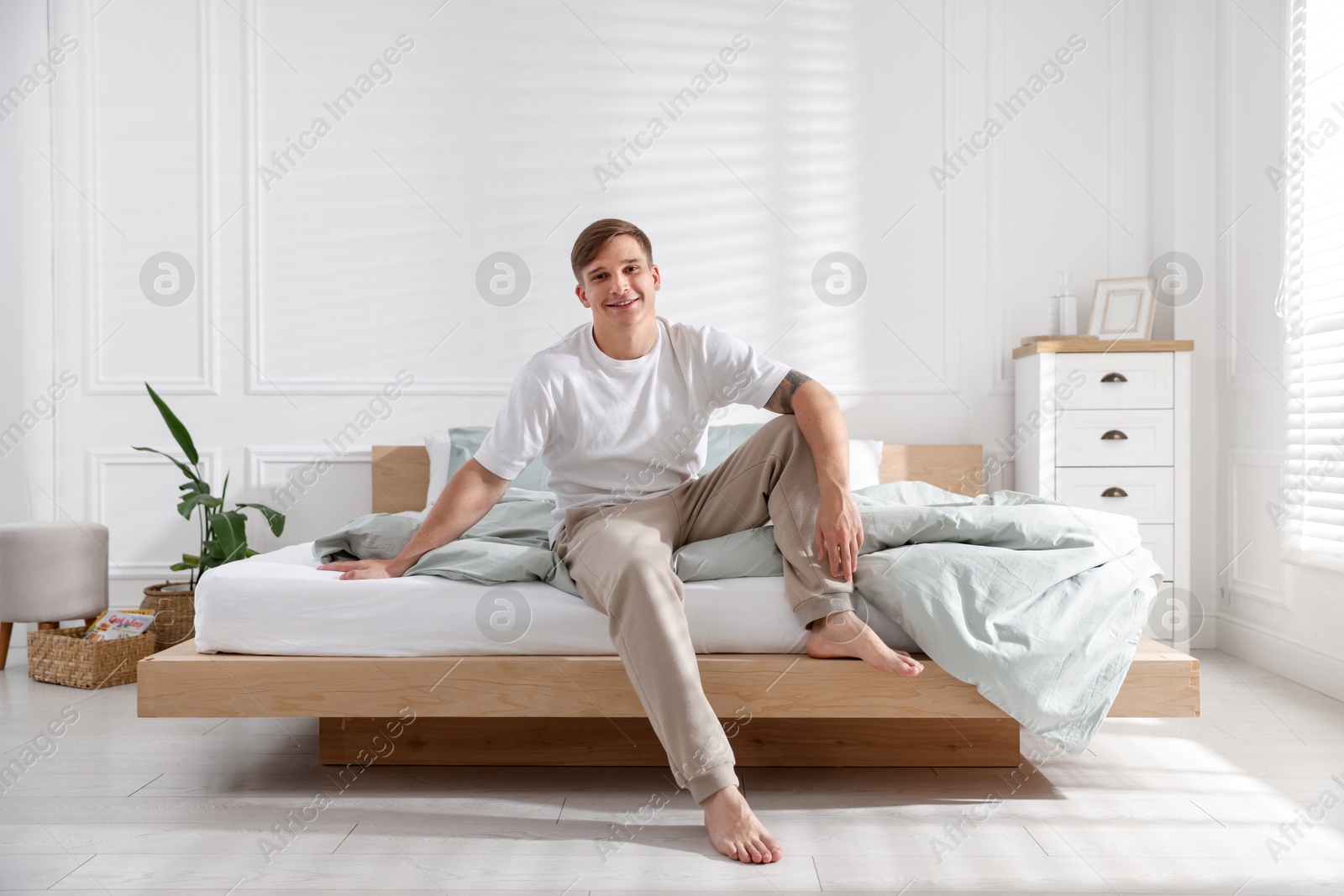 Young man sitting on bed with soft mattress at home Photo of Young man sitting on bed with soft mattress at home