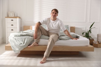 Photo of Young man sitting on bed with soft mattress at home