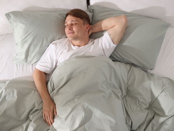 Photo of Young man sleeping on bed with soft mattress at home, top view