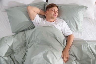 Photo of Young man sleeping on bed with soft mattress at home, top view