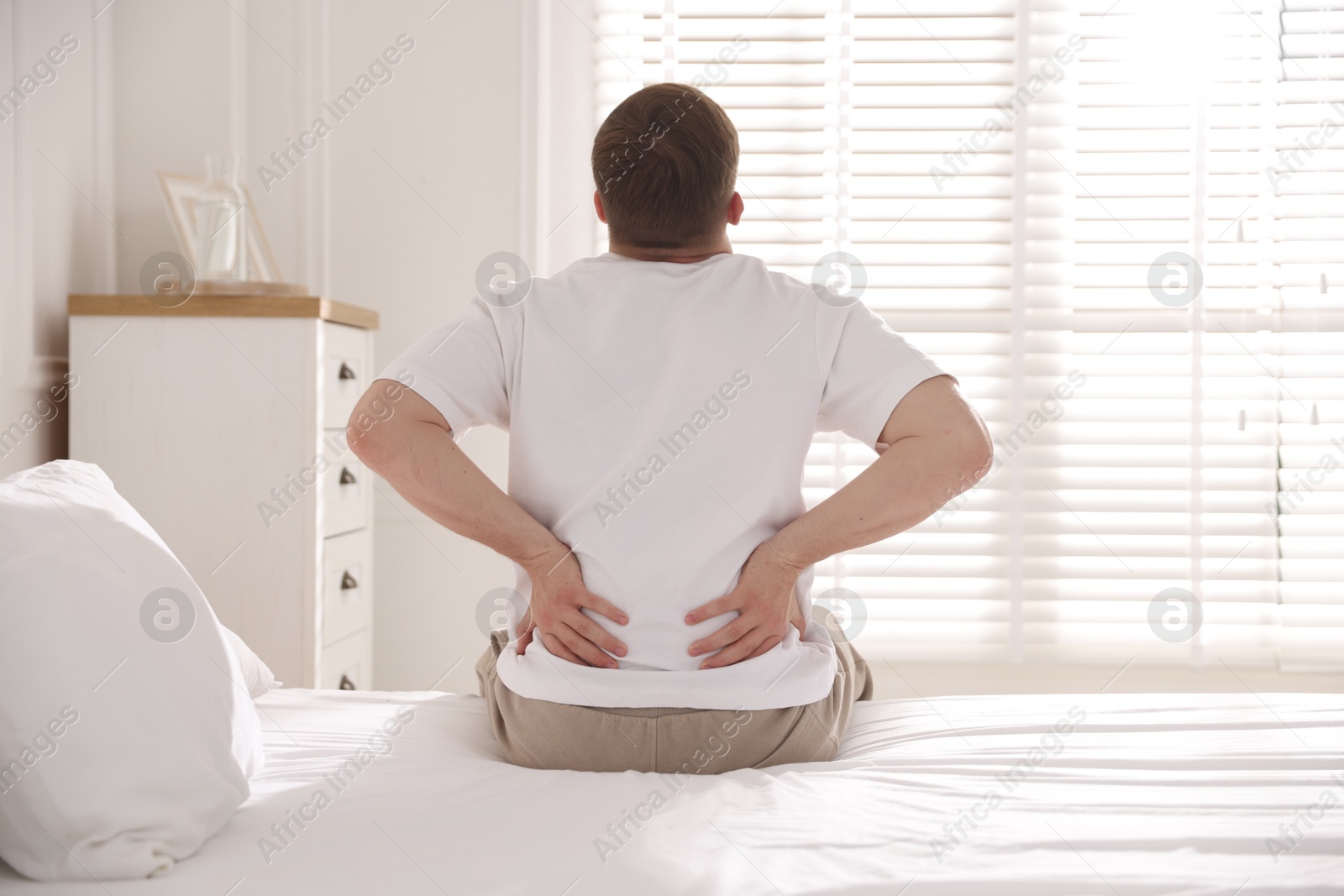 Young man suffering from back pain on bed with soft mattress at home, back view Photo of Young man suffering from back pain on bed with soft mattress at home, back view