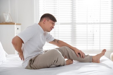 Photo of Young man suffering from back pain on bed with soft mattress at home
