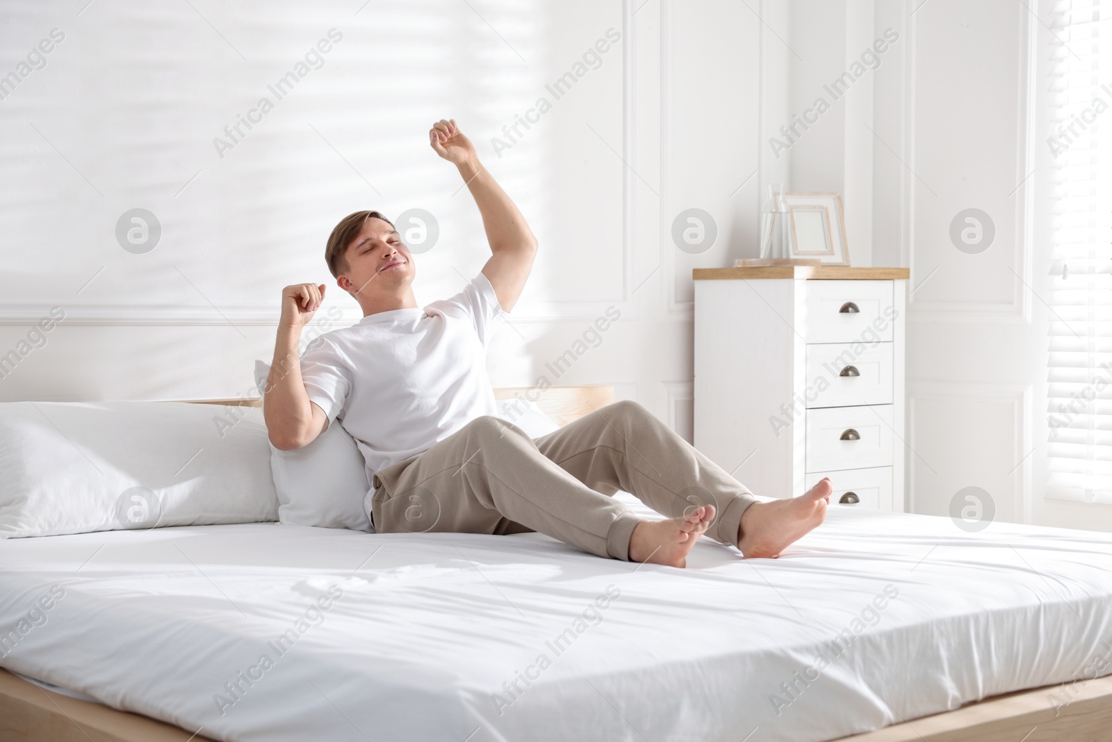 Young man stretching on bed with soft mattress at home Photo of Young man stretching on bed with soft mattress at home