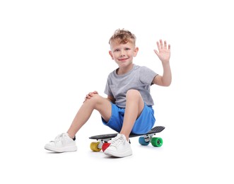 Photo of Little boy sitting on penny board and greeting against white background