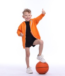 Photo of Cheerful little boy with basketball ball showing thumbs up on white background
