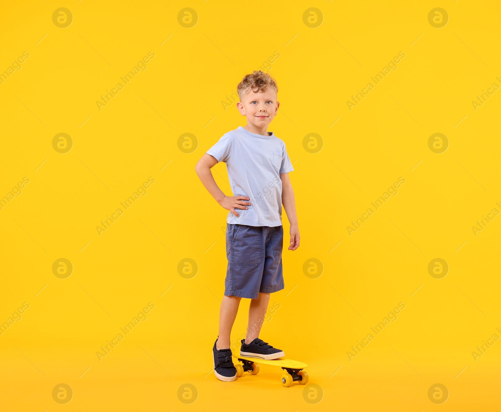 Little boy with penny board on yellow background Photo of Little boy with penny board on yellow background