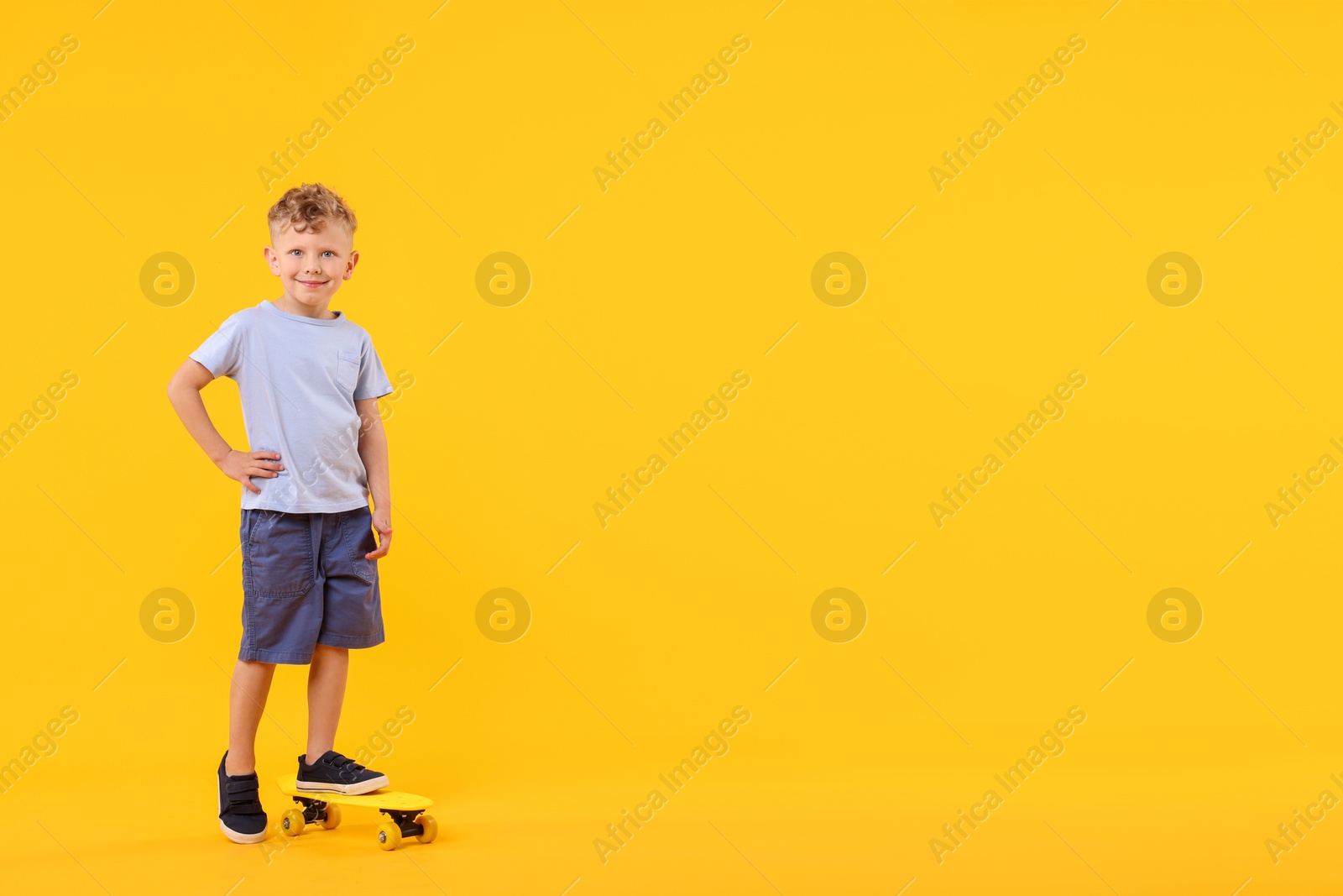 Little boy with penny board on yellow background, space for text Photo of Little boy with penny board on yellow background, space for text