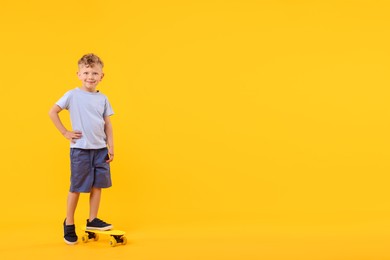 Photo of Little boy with penny board on yellow background, space for text
