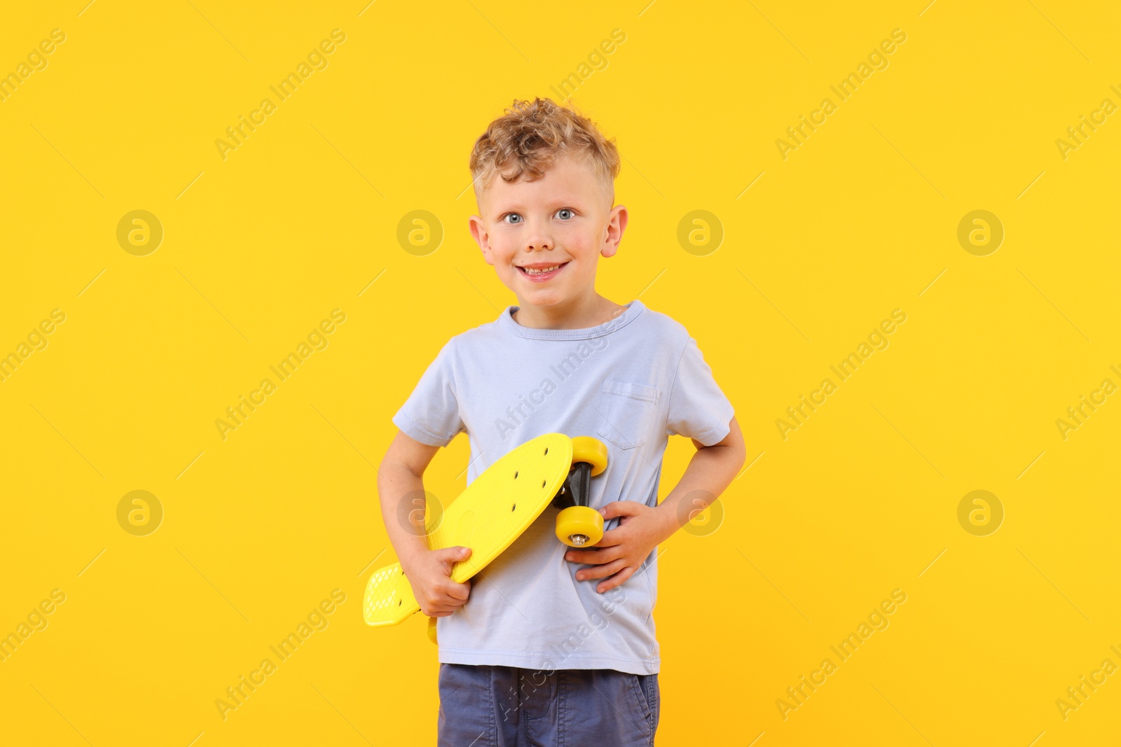Little boy with penny board on yellow background Photo of Little boy with penny board on yellow background
