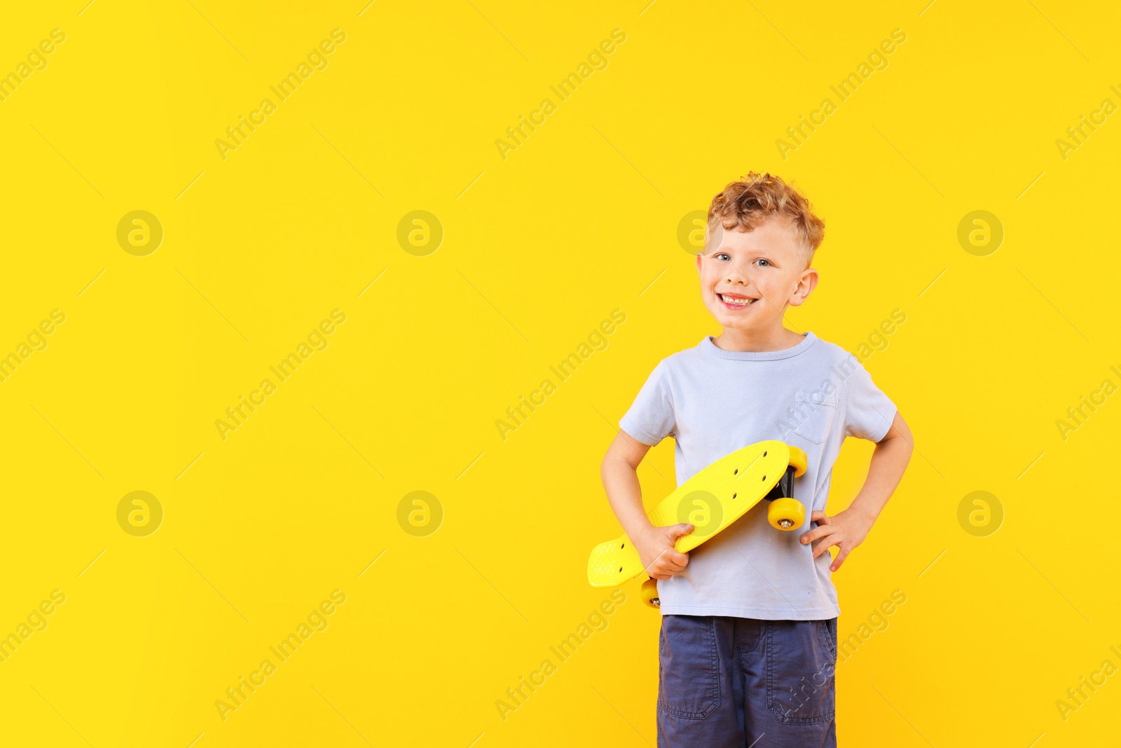 Little boy with penny board on yellow background, space for text Photo of Little boy with penny board on yellow background, space for text