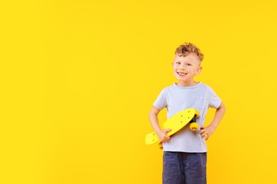 Photo of Little boy with penny board on yellow background, space for text