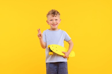 Photo of Little boy with penny board showing V-sign on yellow background
