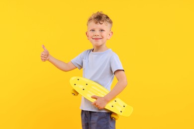 Photo of Little boy with penny board showing thumbs up on yellow background