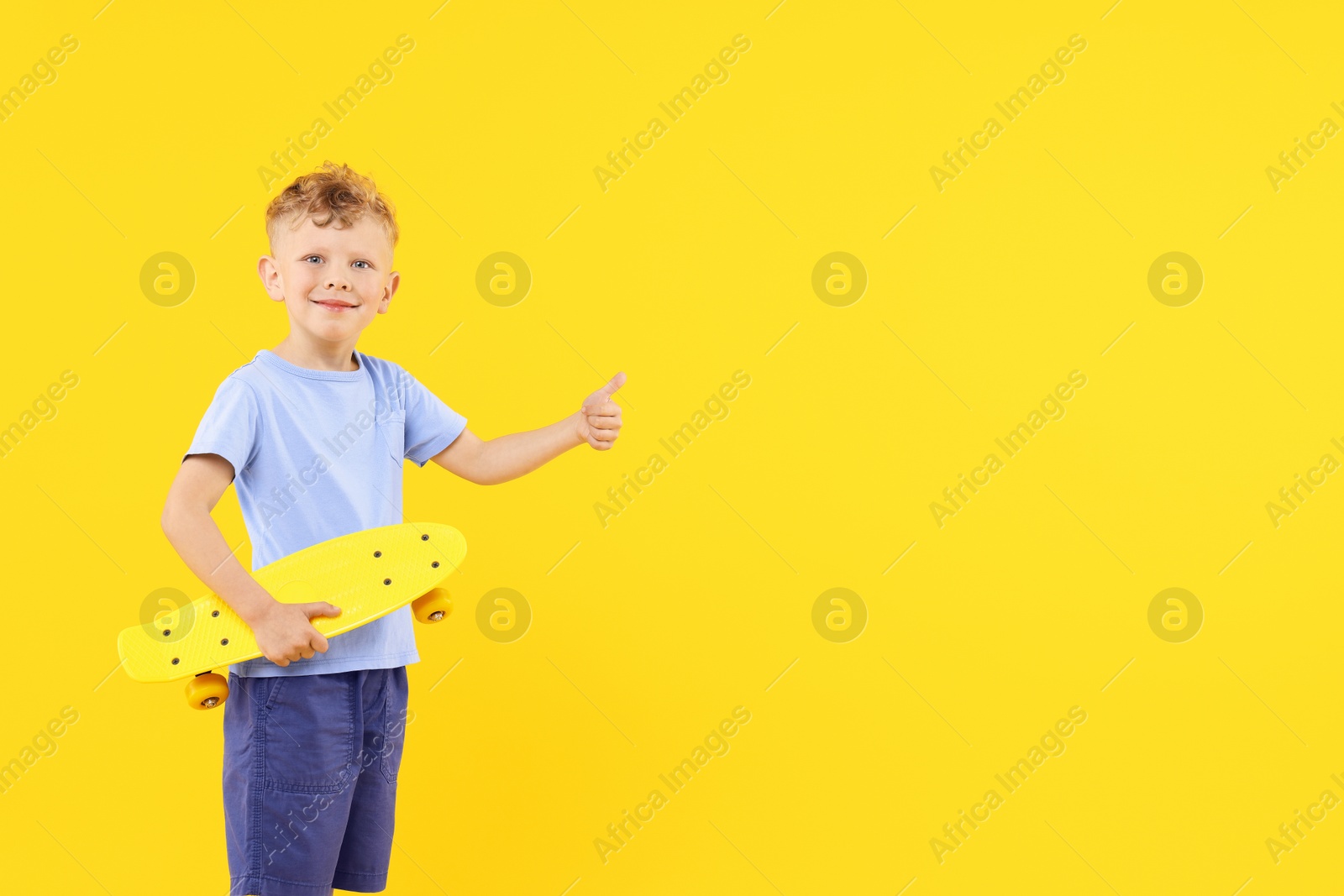 Little boy with penny board showing thumbs up on yellow background, space for text Photo of Little boy with penny board showing thumbs up on yellow background, space for text